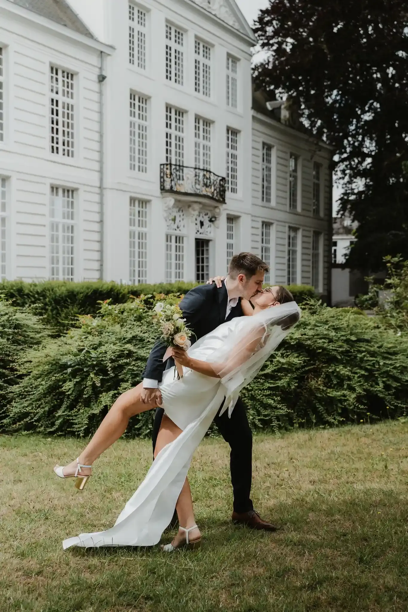 Wedding photography by Bert Van Den Eeckhaut — newlyweds kissing in front of a white building