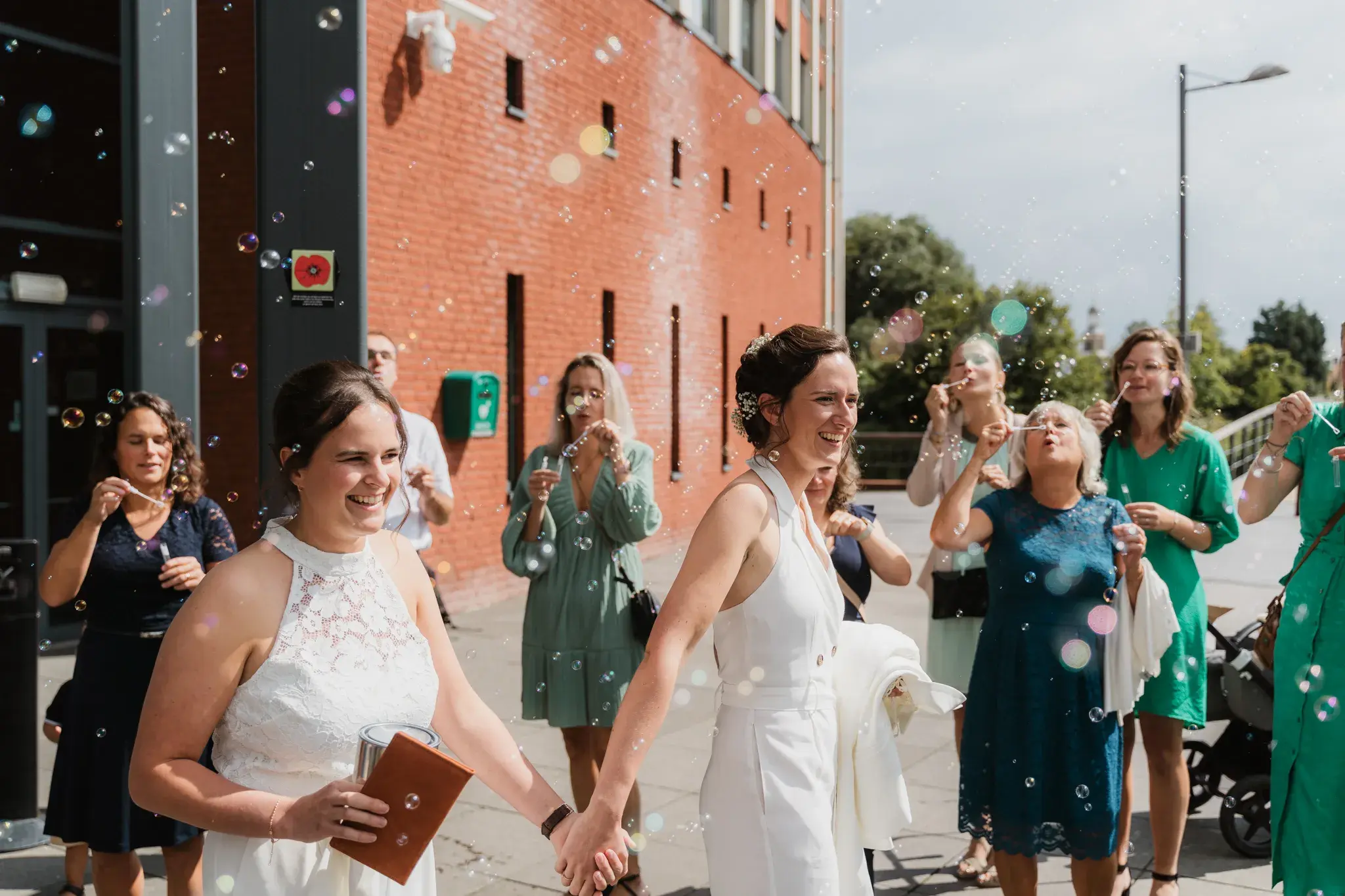 Wedding photography by Bert Van Den Eeckhaut — bride and groom blowing bubbles, wedding party, celebrating, street, daytime